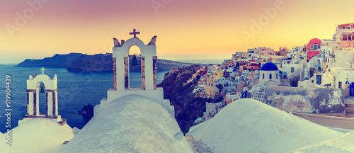 Sunset in Oia town on Santorini island in Greece. Panoramic view of traditional and famous white houses and churches with blue domes over the Caldera, Aegean sea