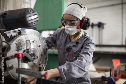 Woman wearing earmuffs and dust mask working on machine