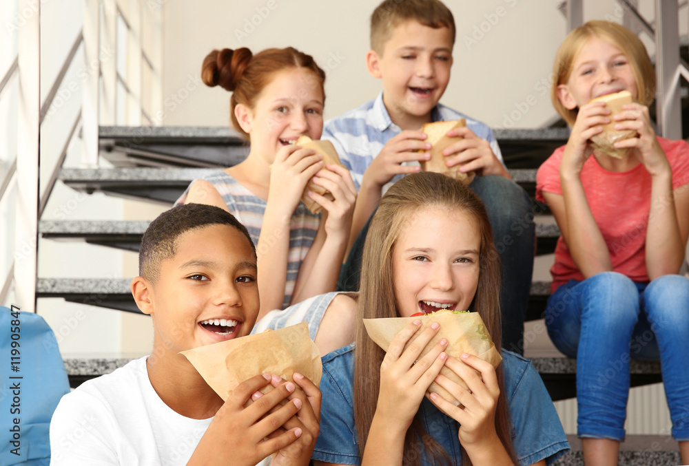 Fototapeta premium Schoolchildren eating sandwiches while sitting on stair-steps at school