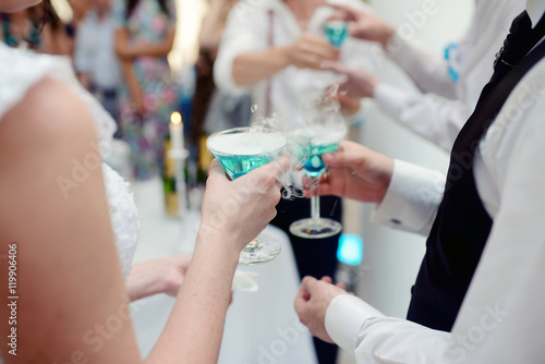 Beautiful wedding couple is pouring champagne indoors. Colorful glasses for alcohol with berries for bride and groom. Beauty of bridal interior for marriage. Bright bar for celebration