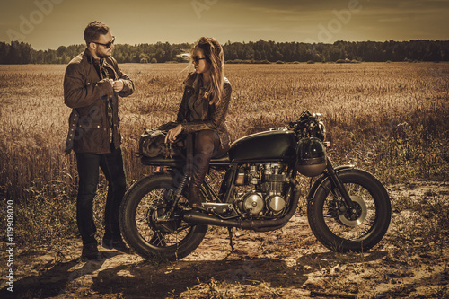 Stylish cafe racer couple on the vintage custom motorcycles in a field.