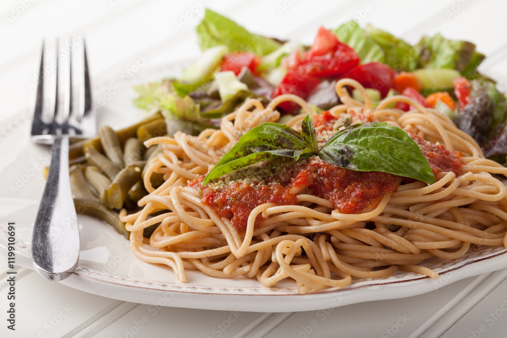 Whole wheat spaghetti topped with organic homemade marinara sauce served with green beans and an Italian side salad side view on white wood Whole wheat spaghetti topped with organic homemade marinara sauce served with green beans and an Italian side salad side view on white wood