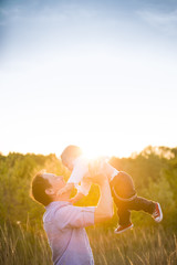 Happy father with his adorable toddler boy son on sunset. Father holding cute baby in the sky on sunny day. Family having fun and enjoying day in the park. Fatherhood, childhood and lifestyle concept