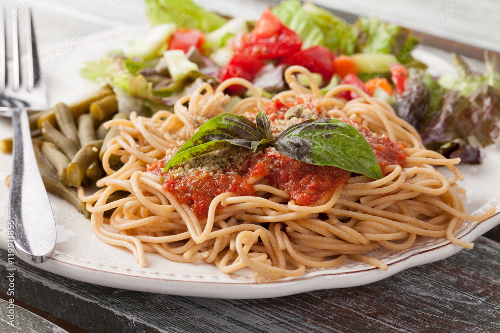 Whole wheat spaghetti topped with organic homemade marinara sauce served with green beans and an Italian side salad on an old weathered barn wood table macro shot