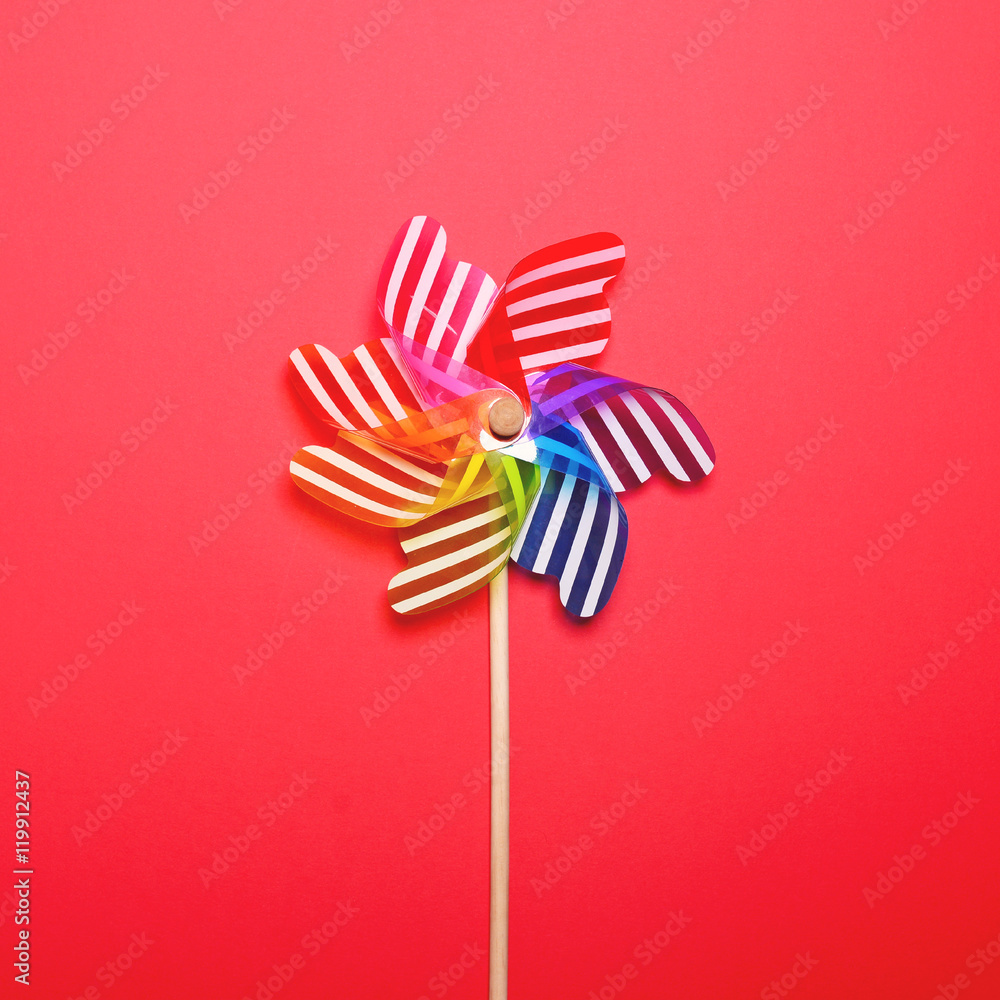 Multicolored pinwheel against red background - Minimal flat lay