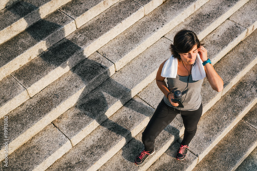 Fitness sporty runner woman listening to music on phone holding cell and bottle of water closing eyes enjoying sunlight for motivation before training workout routine photo