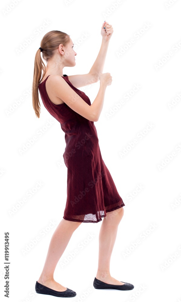 Fototapeta premium back view of standing girl pulling a rope from the top or cling to something. Isolated over white background. A girl in a burgundy dress hanging on a rope ..