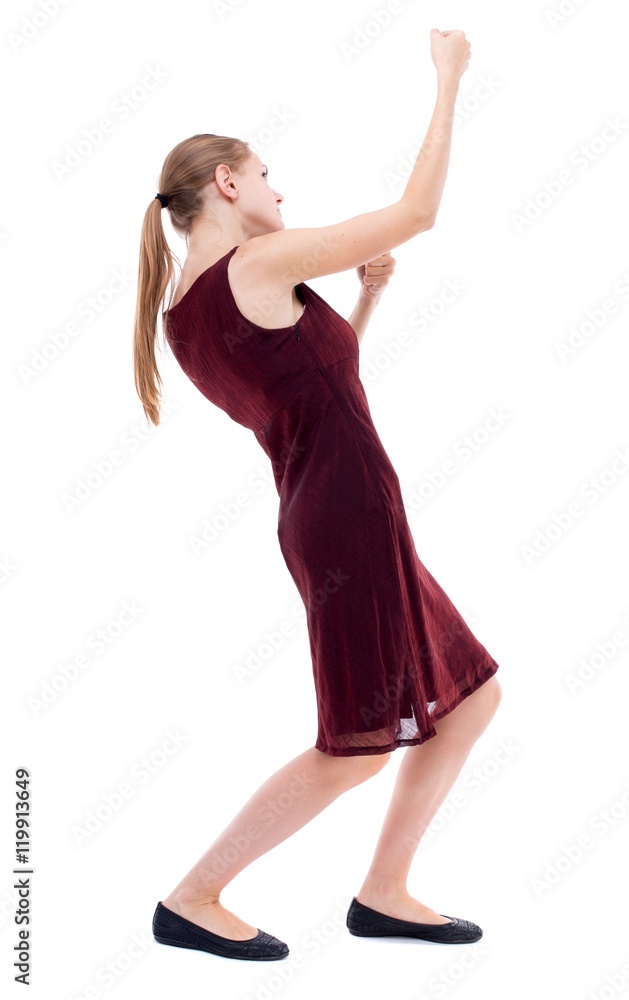 back view of standing girl pulling a rope from the top or cling to something. Isolated over white background. A girl in a burgundy dress pulls the load