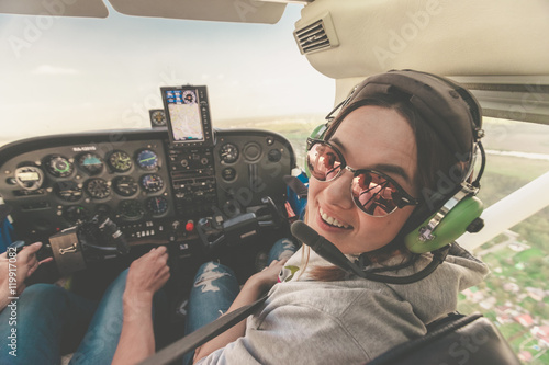 Confident female pilot with headset smiling in the private helicopter. Smiling happy woman wearing headphones and enjoying the flight on a private jet.