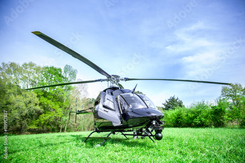 Black with gray stripes helicopter standing on green grass field getting ready to fly over blue sky.