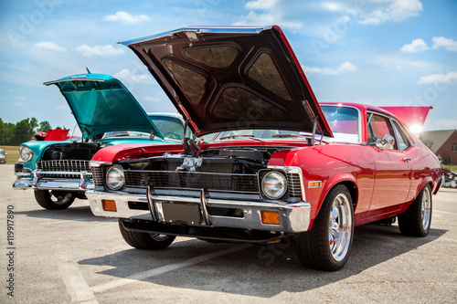 Two old American 70s customized muscle cars with the hoods open on the show