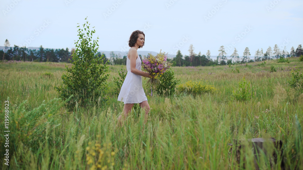 Beautiful inspired woman talking on a blossoming field with a bouquet of wildflowers. Beautiful inspired woman talking on a blossoming field with a bouquet of wildflowers.