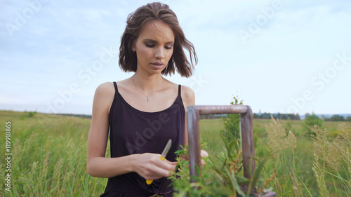 Slim girl in black dress works of flowers at sunset