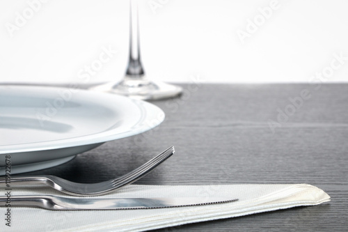 Besteck auf Serviette mit Teller und Weinglas im Hintergrund