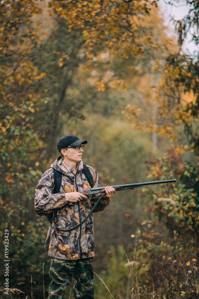 Male hunter in the woods. Man in camouflage with a backpack. Autumn forest, leaf fall.