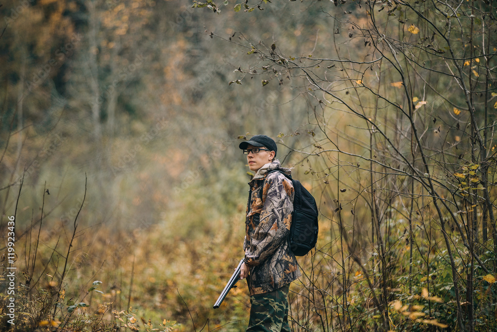 Male hunter in the woods. Man in camouflage with a backpack. Autumn forest, leaf fall.
