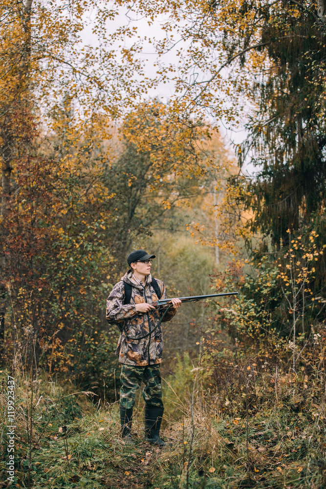 Male hunter in the woods. Man in camouflage with a backpack. Autumn forest, leaf fall.