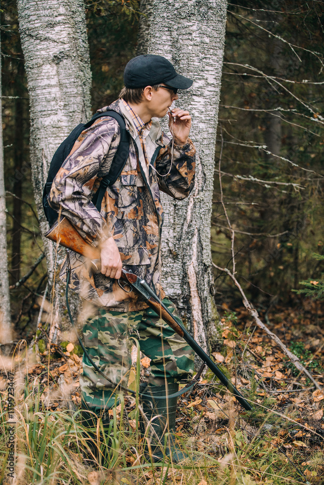 Male hunter in the woods. Man in camouflage with a backpack. Autumn forest, leaf fall.