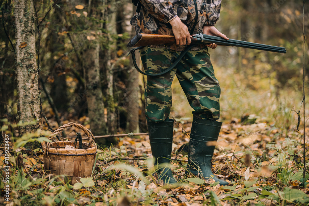 Naklejka premium Male hunter in the autumn forest. A man holding a gun.