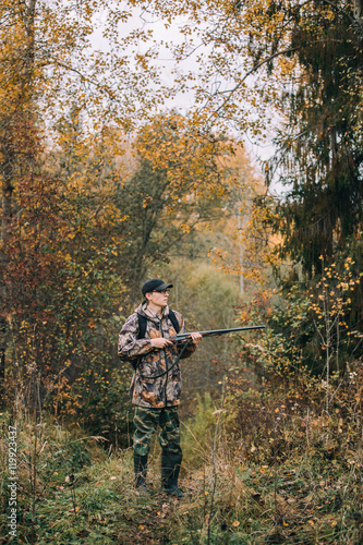 Male hunter in the woods. Man in camouflage with a backpack. Autumn forest, leaf fall.