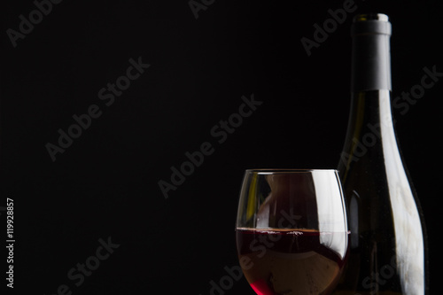 Red wine in a glass and bottle on a dark black background