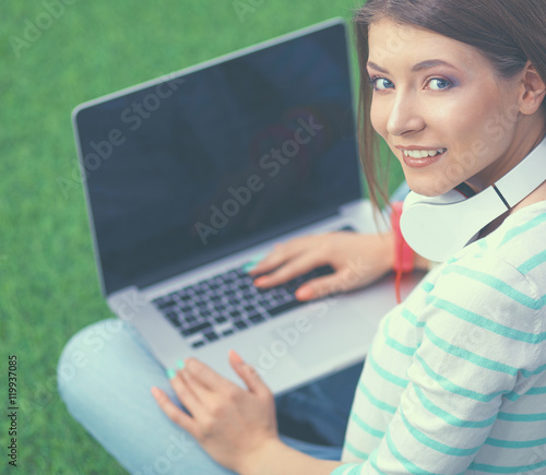 Young woman with laptop sitting on green grass 