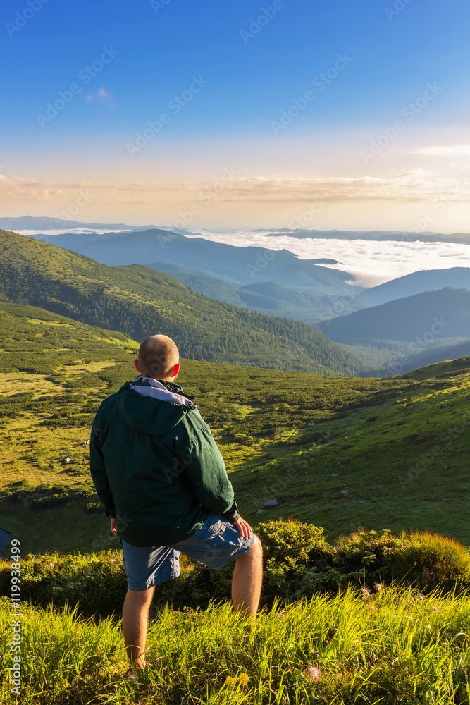 Young man standing on the top of mountain and looking at beautiful mountain landscape in sunrise time, Carpathians.