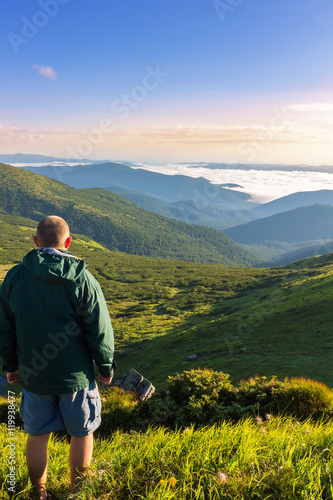 Young man standing on the top of mountain and looking at beautiful mountain landscape in sunrise time, Carpathians. © O.Farion