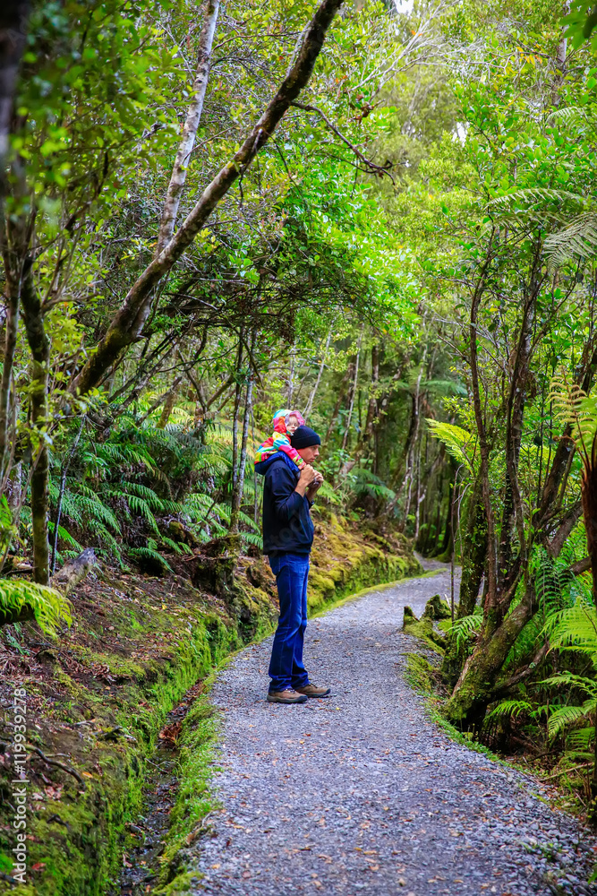 Father is carrying little daughter on his shoulders. Haast, South Island, New Zealand