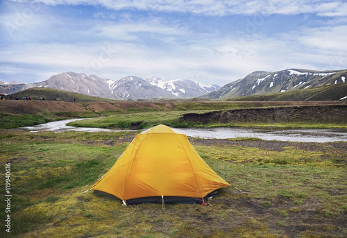 An orange tent on a river shore   camping and trekking in Iceland