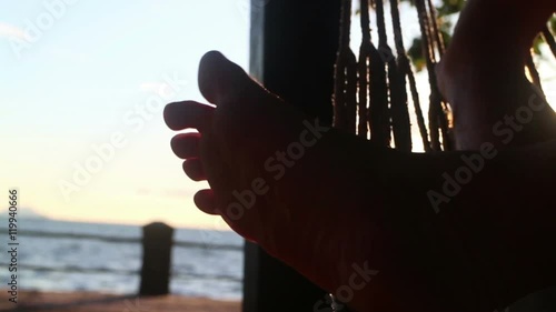 Extreme close up of foot of person relaxing in a hammock near the sea, with sun intermittently flashing between the toes as they swing. (POV is of person lying in the hammock).  photo