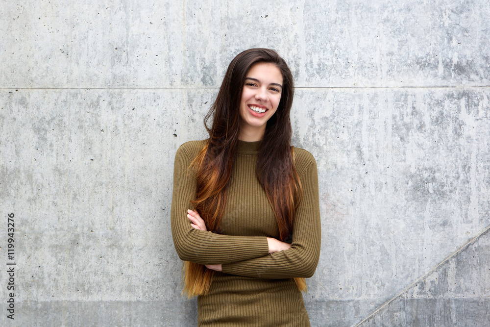 Happy young woman leaning against gray wall