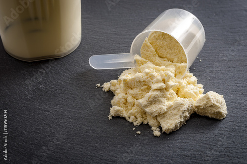 Fitness and sports concept with a spilled scoop of protein powder necessary nutrition for muscle recovery after an intensive workout, next to a protein shaker