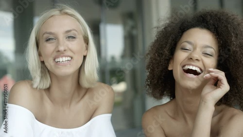 Two cute multiracial girls lauging in cafe restaurant, outdoors. Sunny day/summer.