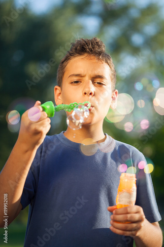 boy blowing soap bubbles in summer park