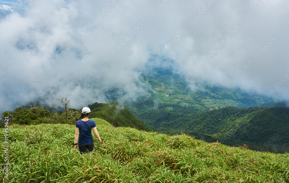 A young woman stands in the grass field on top of mountain. A tourist appreciate with view point on the mountain peak. A young woman stands in the grass field on top of mountain. A tourist appreciate with view point on the mountain peak.