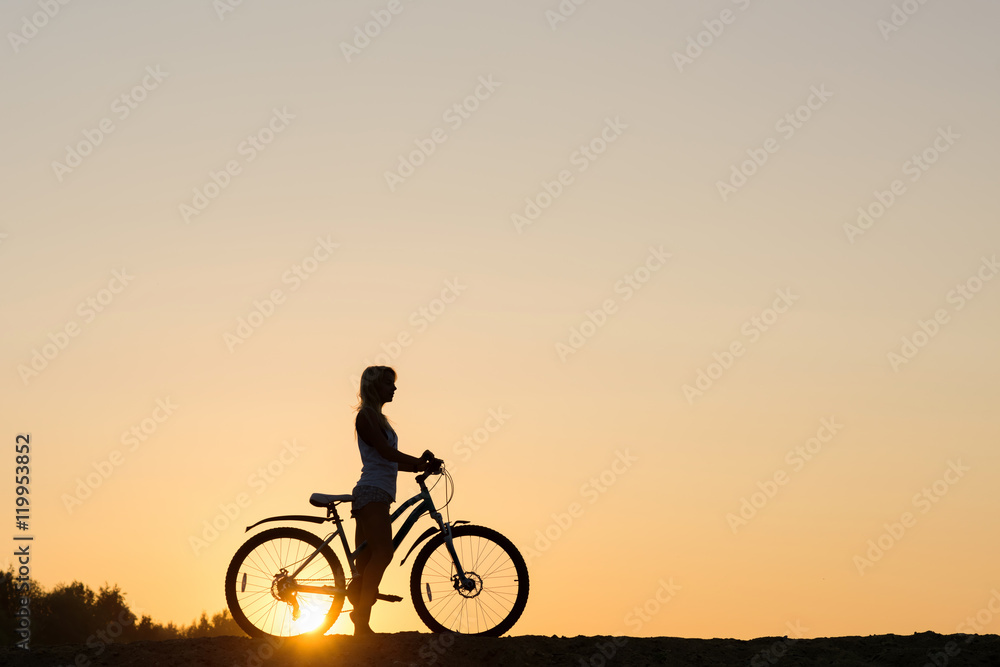 Silhouette of a woman with her bicycle on the beach. You only live once!