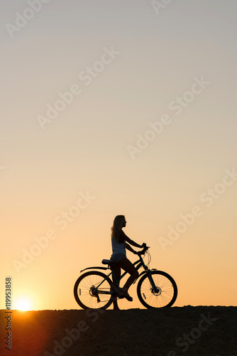 Silhouette of woman with her bicycle on sunset background. My sunset exercise