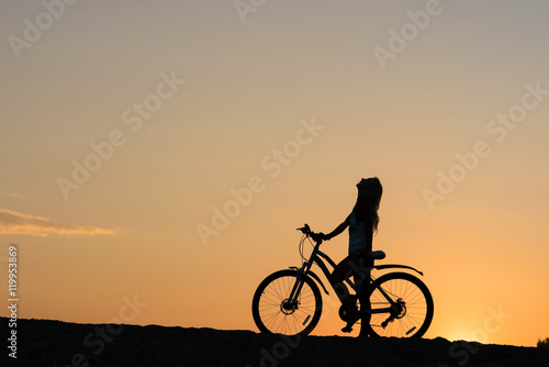 Silhouette of a woman with her bicycle on the beach. Lonely sunset cyclists