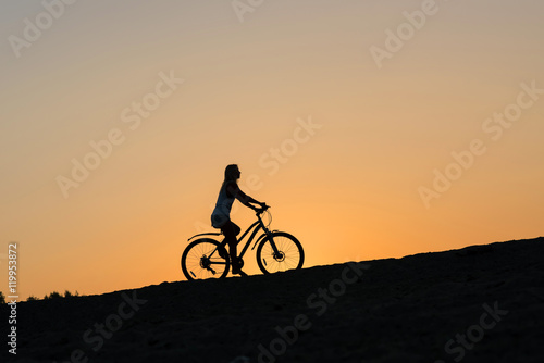 A silhouette of a female cyclist on the beach at sunset. Cycling off into the sunset