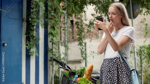 Pretty girl using smartphne as a mirror and painting her lips, steadycam shot
 photo