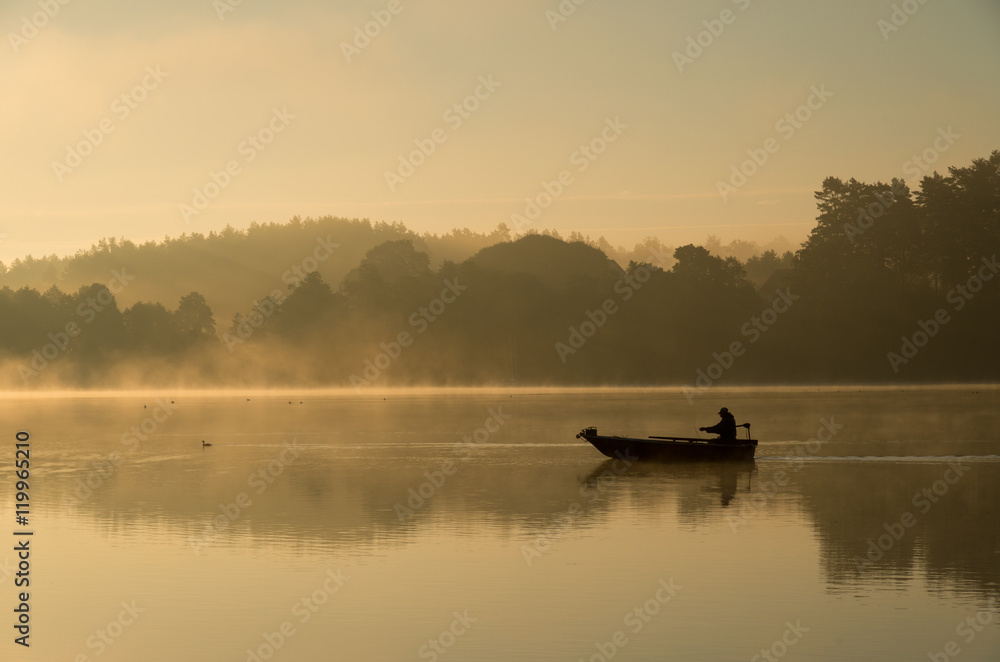 Człowiek wędkujący na łódce mglisty, złoty poranek.