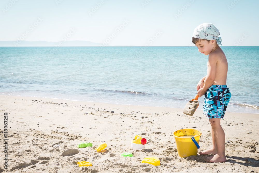 Caucasian child playing on the beach with pail and shovel in summertime Caucasian child playing on the beach with pail and shovel in summertime