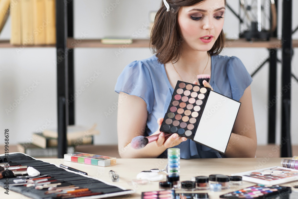 Fototapeta premium Cosmetics consult tells about eyeshadows palette. Young woman holding colorful eye cosmetics swatch. Makeup, beauty, fashion concept