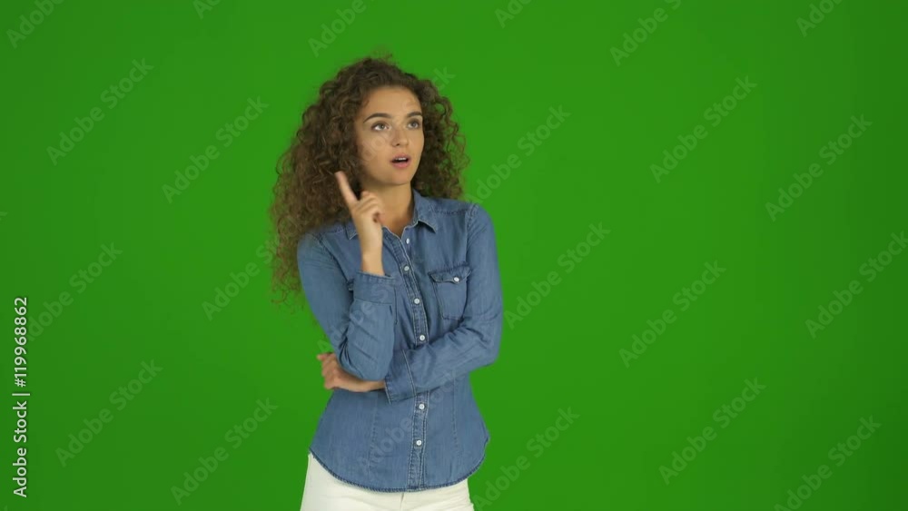 The young curly woman get an idea and stand on the green background. Real time The young curly woman get an idea and stand on the green background. Real time