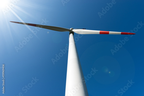 Detail of a white and red wind turbine with sun rays on a clear blue sky 