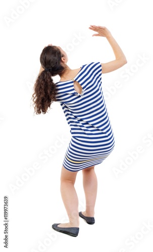 back view of woman protects hands from what is falling from above. Swarthy girl in a checkered dress frightened of something on top.