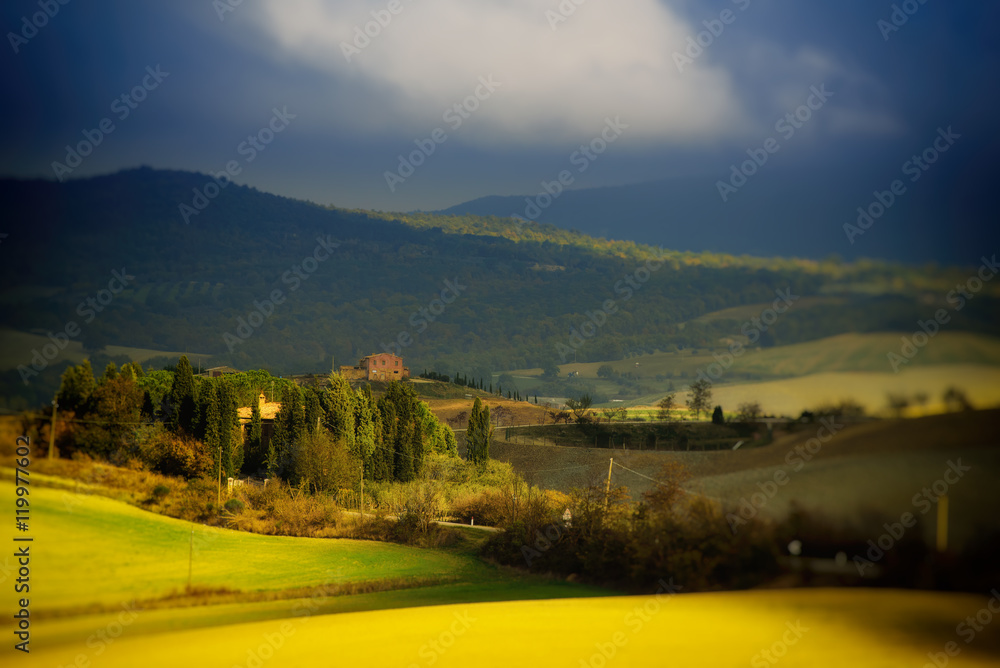 Wavy fields in Tuscany with shadows and farms, Italy. Natural outdoor seasonal spring background with blue dramatic sky and clouds.