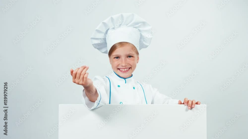 Chef girl in uniform 7-8 years behind the whiteboard and has hand near face smiling at camera. Isolated on white Chef girl in uniform 7-8 years behind the whiteboard and has hand near face smiling at camera. Isolated on white