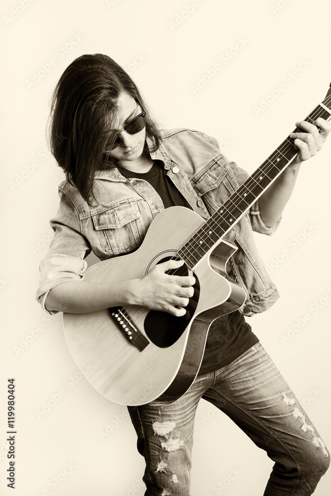 Fashion portrait of a teenager playing guitar in studio wearing jeans jacket Fashion portrait of a teenager playing guitar in studio wearing jeans jacket
